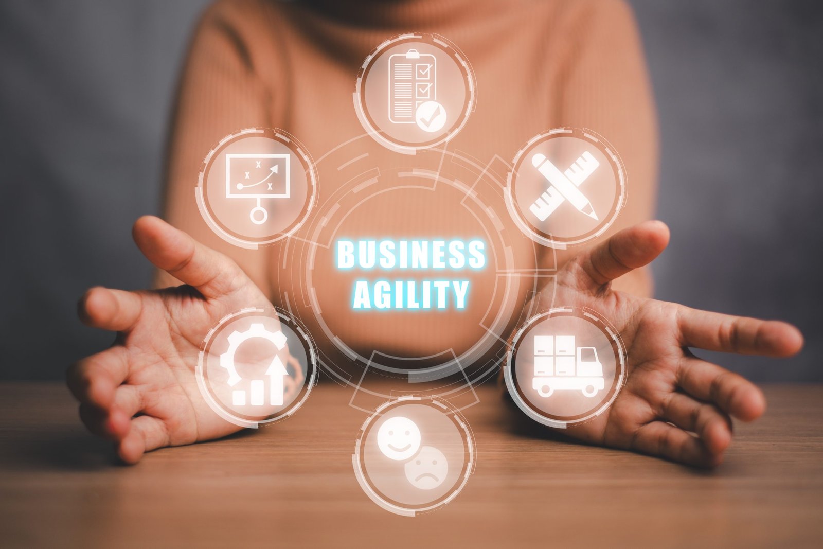 A person holding out both hands beneath a glowing "Business Agility" graphic ringed by icons for planning, quality, strategy, delivery, customer sentiment and continuous improvement.